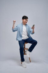 Happy excited Asian man looking at his smartphone and raising his arm up to celebrate success