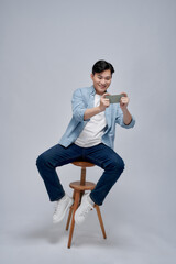Portrait of an excited young man sitting on a stool and playing games on mobile phone