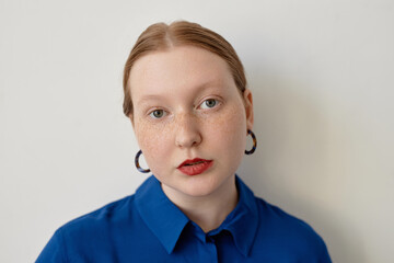 Minimal portrait of creative red haired woman looking at camera wearing red lipstick, copy space