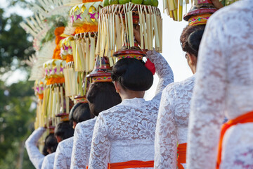 Procession of beautiful Balinese women in traditional costumes - sarong, carry offering on heads...