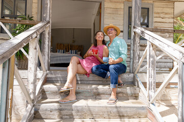 Carefree caucasian senior couple with coffee cups sitting on steps and relaxing outside cottage