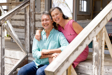 Caucasian senior couple smiling cheerfully and sitting on staircase outside cottage