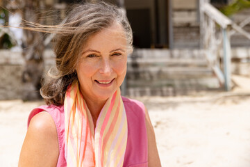 Close-up portrait of smiling caucasian senior woman with scarf around neck sitting at beach