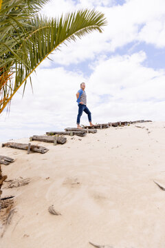 Low Angle View Of Caucasian Senior Man Standing On Boardwalk At Sandy Beach Against Cloudy Sky