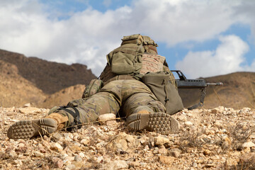 Un soldado armado de uniforme vigila sobre una loma del desierto.