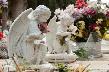 Fototapeta na wymiar Vista de dos angelitos arrodillados sosteniendo flores orando por algún difunto.