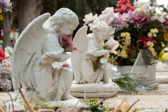 Vista de dos angelitos arrodillados sosteniendo flores orando por alg&uacute;n difunto.