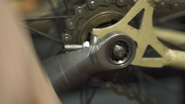 A bicycle mechanic tightening the rear wheel axle screw of a bicycle wheel.