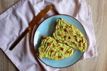 Turquoise plate with two pieces of avocado toast on wooden table. Top view.