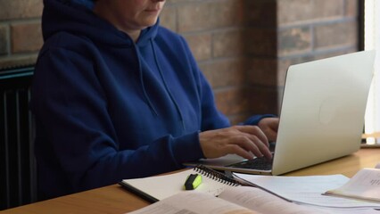 female freelancer student sitting brown table typing keyboard opened laptop, textbooks, books on table. back to school, distant education, online working, freelance concept. unrecognizable woman hands - Powered by Adobe
