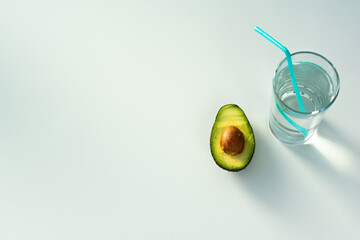 halves of fresh ripe avocado and pure water in a glass with a straw on a white table - the concept of healthy eating