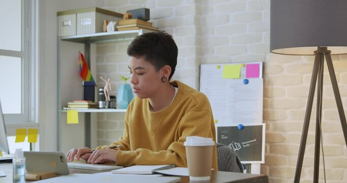 Young Asian tomboy woman in casual attire working from home on laptop computer in living room