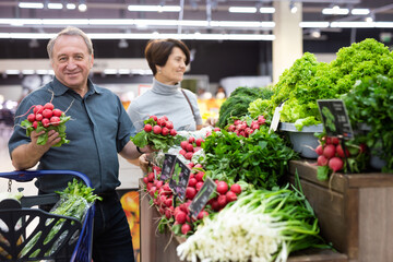 Smiling happy couple is choosing bell peppers and other vegetables in supermarket