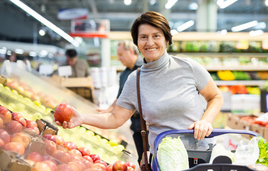 Positive woman chooses ripe red apples on grocery store window