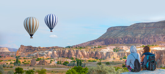 Hot air balloon flying over spectacular Cappadocia - Girls watching hot air balloon at the hill of...
