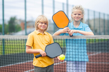 Portrait smiling pickleball game players boy and girl with yellow ball and paddles, outdoor sport...