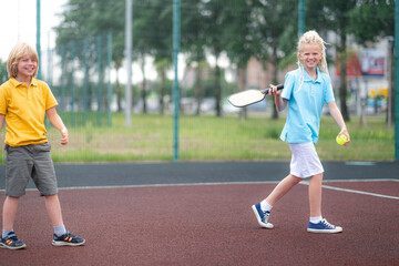 Laughing boy and girl playing pickleball game, hitting pickleball yellow ball with paddle, outdoor...