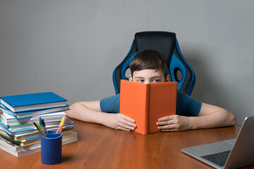 school boy reading and hide behind book at home