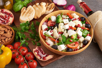 Greek salad or horiatiki with large pieces of tomatoes, cucumbers, onion, feta cheese and olives in white bowl isolated top view. Village salad with diced mozzarella, arugula, parsley and olive oil