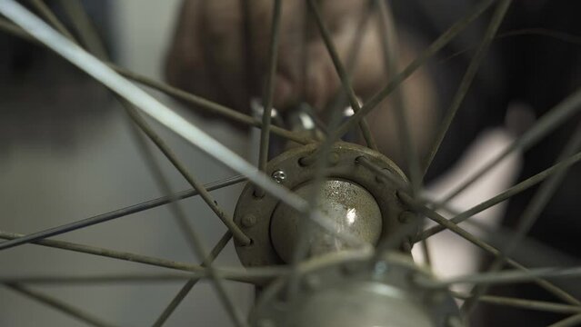 A bicycle mechanic installing a new spoke on a wheel hub.