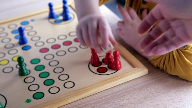 close-up of hands of small child manipulate with wooden figurines of family board game, smart kid, 2-year-old girl is learning to count, Cross and circle game Parcheesi, foreground focus