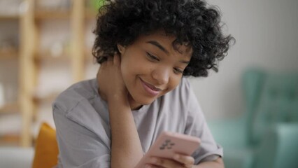 Smiling falling in love african american girl dreaming enjoying reading message in smartphone sitting on sofa at home. Online dating, romantic relationship, cute communication with boyfriend concept.