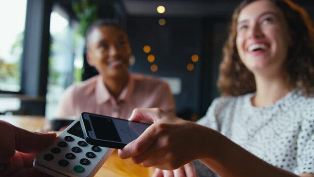 Woman in coffee shop paying bill with contactless mobile phone payment - shot in slow motion