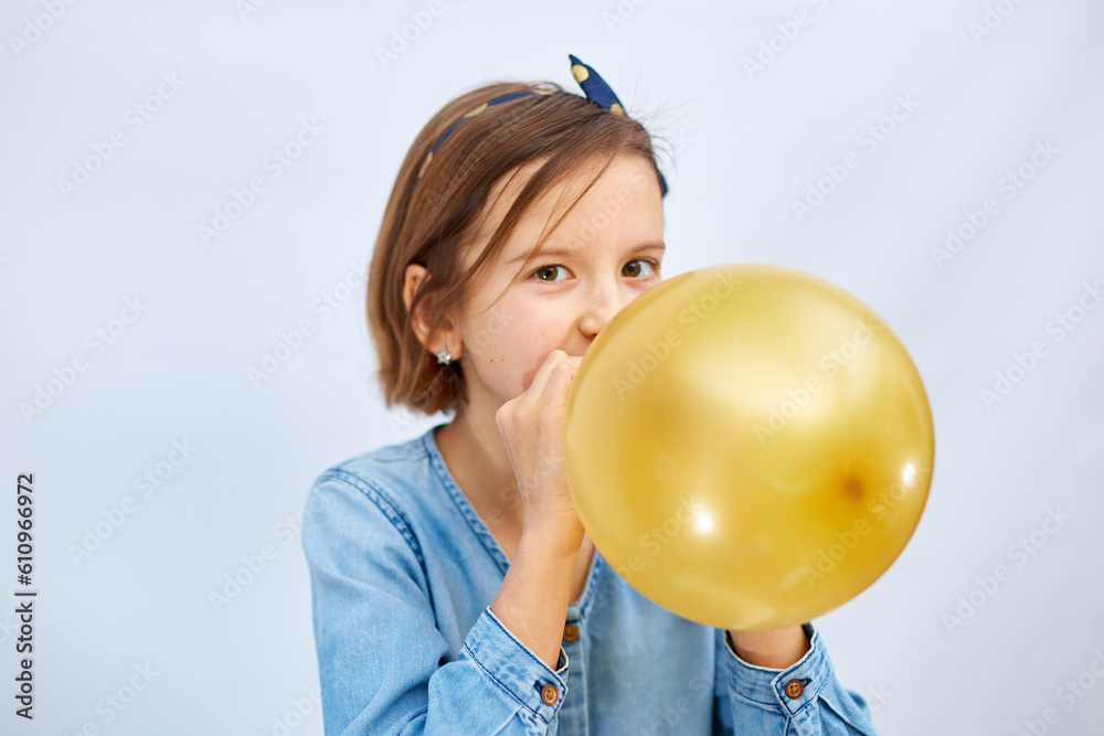 Wall mural pretty little girl in casual denim dress blowing, inflate yellow balloon