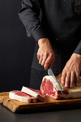 Chef cuts steak in the kitchen, dark background, various spices(Rosemary, garlic, butter, pepper, salt and other spices),close up