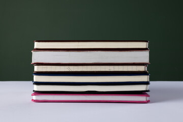 Close up of stack of books and notebooks with copy space on green background
