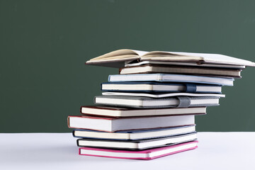 Close up of stack of books and notebooks with copy space on green background