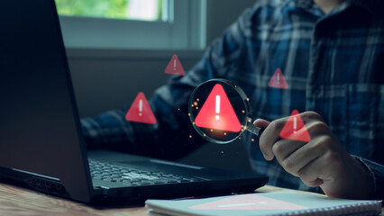 Hand holding magnifier glass with red triangle caution warning sign for notification error and...