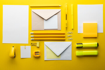 Flat lay of yellow pencils, pen and highlighter and white paper with copy space on yellow background