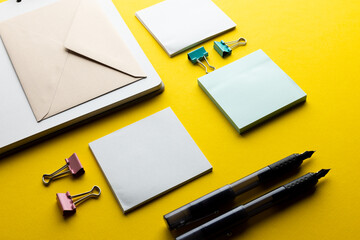 Flat lay of black pens, envelope and white paper with copy space on yellow background