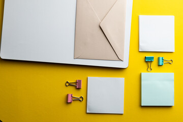 Flat lay of memo notes, paper clips, envelope and white paper with copy space on yellow background