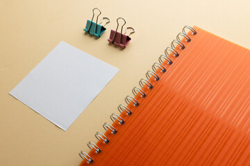 Flat lay of orange notebook, memo note and paper clips with copy space on yellow background