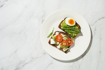 Breakfast with toast, avocado, eggs and vegetables on a gray background