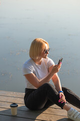 Young beautiful woman drinking coffee and talking on the phone near the river in the park