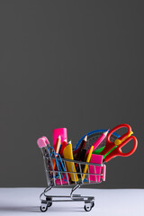 Close up of miniature shopping trolley with school materials and copy space on grey background