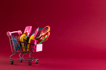 Close up of miniature shopping trolley with school materials and copy space on red background
