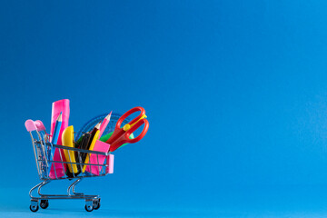 Close up of miniature shopping trolley with school materials and copy space on blue background