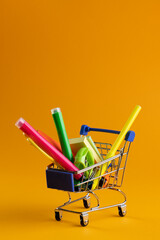 Close up of miniature shopping trolley with school materials and copy space on orange background