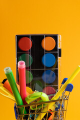 Close up of miniature shopping trolley with school materials and copy space on orange background