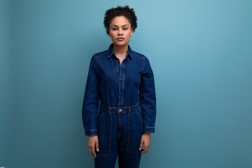 portrait of a young woman with dark skin and black curly hair dressed in blue denim overalls...