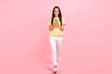 Fototapeta na wymiar Full length photo of shiny cute woman dressed yellow t-shirt walking chatting iphone modern device isolated pink color background