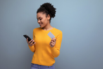 pretty young hispanic woman with black curly hair in a yellow sweater on online shopping with a...