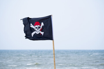 Un drapeau de tête de mort pirate qui flotte sur une plage face à la mer