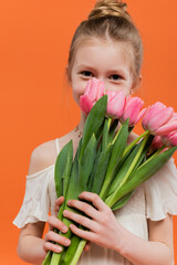 preteen girl in white sun dress holding pink tulips on orange background, fashion and style concept, bouquet of flowers, fashionable kid, vibrant colors, covering face