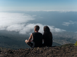 romantic lovely couple sitting on mountain top above clouds and looking on view - Powered by Adobe