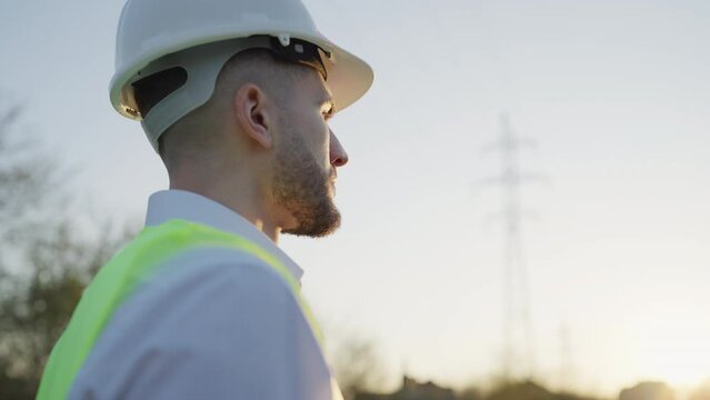 Side View of Handsome Engineer Putting on his Safety Gear Helmet at Job Site. Outdoors. Worker Stranding in the Power Plant. Emphasizing Maintenance, Service, Construction Industry